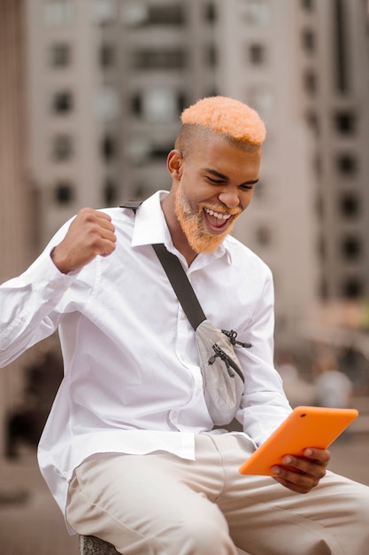 Uma foto de um homem com o cabelo tingido e um tablet nas mãos