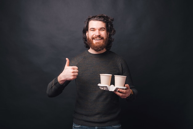 Uma foto de um homem sorrindo e segurando duas xícaras de bebidas quentes agradecendo por sua qualidade