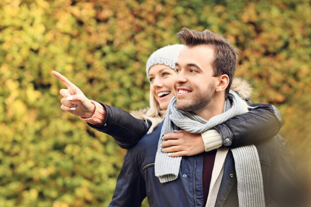 Uma foto de um jovem casal romântico apontando para algo no parque no outono