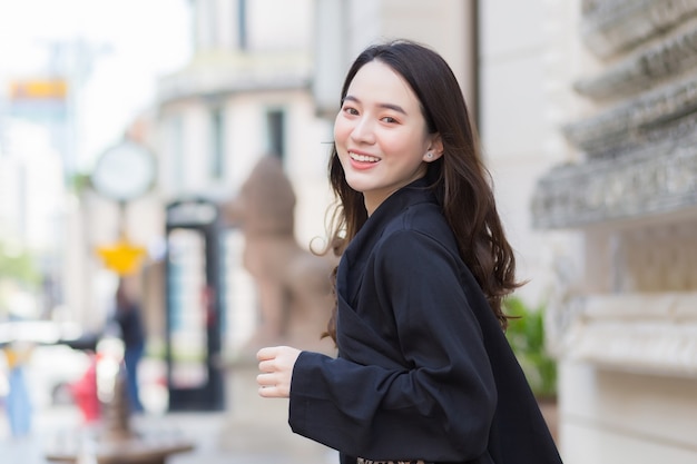 Uma foto de uma linda mulher asiática de cabelos compridos em uma túnica preta sorrindo feliz caminhando