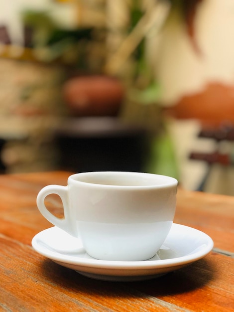Uma foto linda de uma xícara de café expresso em branco em uma mesa de madeira com um fundo desfocado
