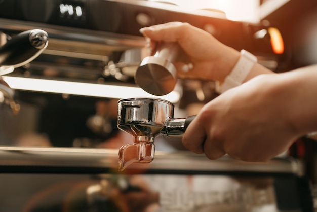 Uma foto perto de mãos que detém uma adulteração de metal e um porta-filtro com café em uma cafeteria