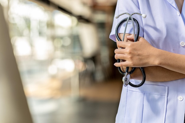 Foto uma fotografia de um médico em pé com os braços cruzados segurando um estetoscópio em um fundo desfocado do interior do hospital. o conceito de um curador.