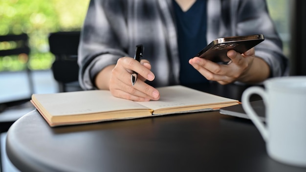 Uma freelancer asiática usando seu smartphone e tomando notas em seu notebook