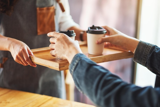 Uma garçonete segurando e servindo copos de papel com café quente para um cliente no café