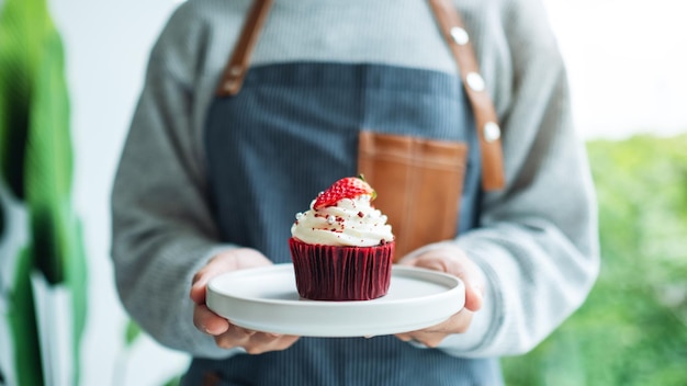 Foto uma garçonete segurando e servindo um pedaço de cupcake de veludo vermelho