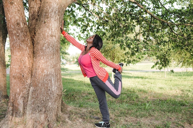 Uma garota afro-americana que pratica esportes fez um aquecimento enquanto segurava uma árvore com a mão.