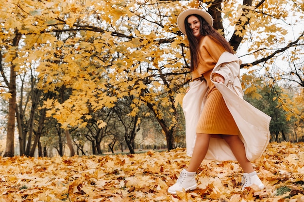 Foto uma garota alegre em um casaco branco e um chapéu sorri em um outono park.portrait de uma mulher sorridente no outono dourado.