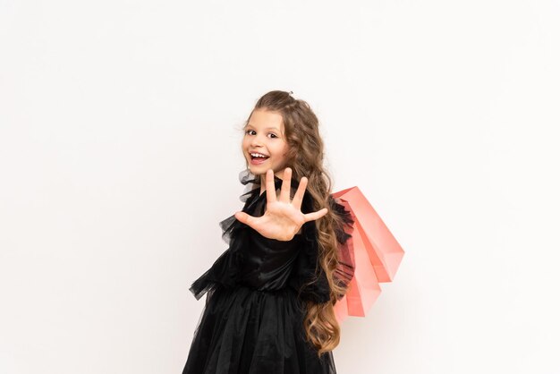 Uma garota alegre em um vestido segura uma sacola de compras na Black Friday Compras para uma princesinha com cabelos cacheados em um fundo branco isolado