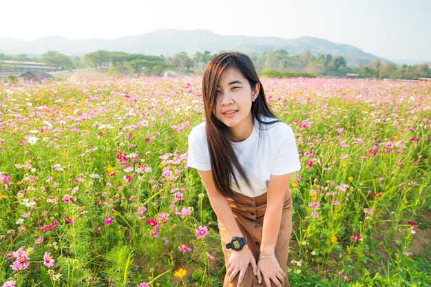 Uma garota asiática vestindo um vestido branco usando um chapéu alegre em um campo de cosmos colorido com