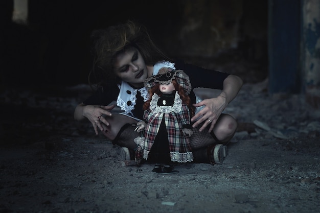 Foto uma garota assustadora com uma boneca no chão em uma casa abandonada. uma ideia para o halloween