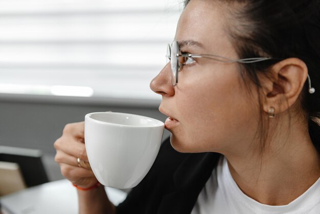 Uma garota bebe café no escritório e pensa que uma garota está pensando em uma pausa no trabalho do funcionário
