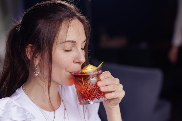 Uma garota bebe um coquetel negroni no terraço de um restaurante moderno