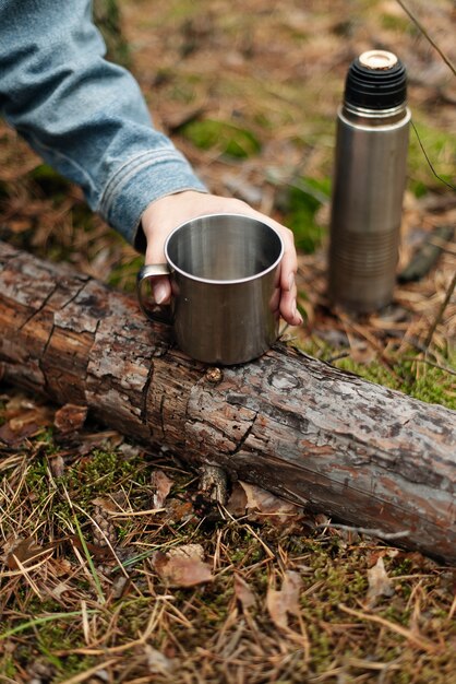 Uma garota bebendo chá em uma garrafa térmica. Chá da garrafa térmica na floresta. Bebendo da garrafa térmica. A atmosfera da floresta.