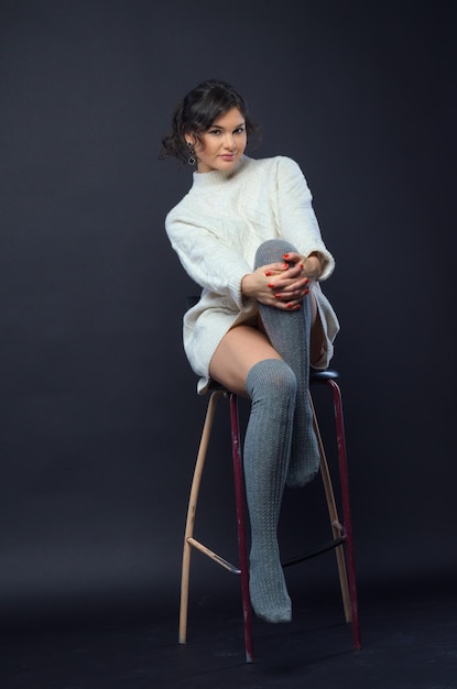 Uma garota bonita em um estúdio escuro com uma camisola branca senta-se em uma cadeira