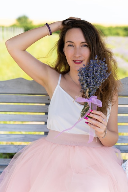 Foto uma garota bonita em um vestido com um buquê de flores de lavanda senta-se em um banco