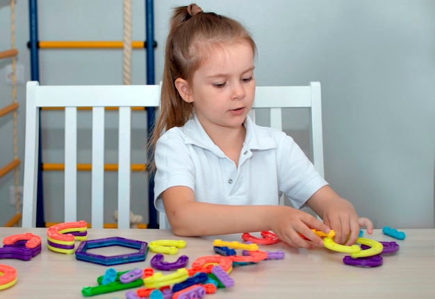 Uma garota brinca com o construtor de brinquedo na mesa da sala. Conceito e aprendizagem por meio de atividades lúdicas para o desenvolvimento infantil.