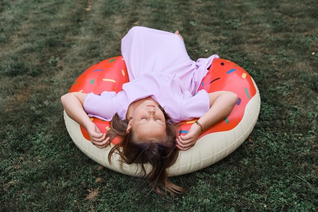 Uma garota brinca com um círculo inflável com um dout no jardim em um dia quente de verão.