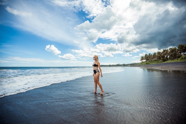 Uma garota caminha ao longo de uma praia de areia preta em bali