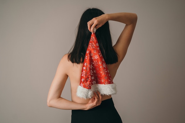 Uma garota com as costas nuas em um chapéu de natal. lugar para texto de ano novo.