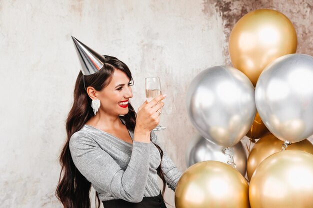 Uma garota com balões está rindo no contexto de uma parede decorativa Uma linda mulher feliz no aniversário de uma festa de ano novo se divertindo segurando uma taça de champanhe