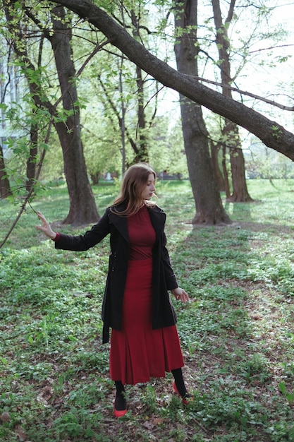 Foto uma garota com cabelo loiro no golfe vermelho e uma saia caminha pela floresta de primavera