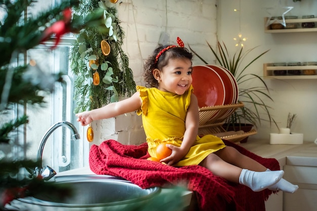 Uma garota com cor de pele escura, ela está sentada na mesa usando um vestido amarelo e segurando laranjas