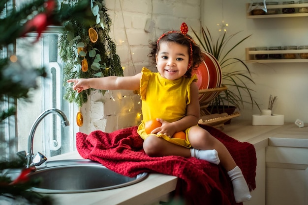 Uma garota com cor de pele escura, ela está sentada na mesa usando um vestido amarelo e segurando laranjas