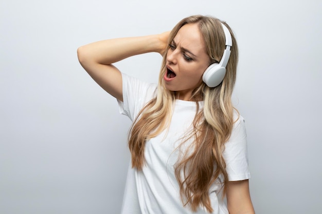 Uma garota com entusiasmo e alegria no rosto ouve música em grandes fones de ouvido brancos em um branco