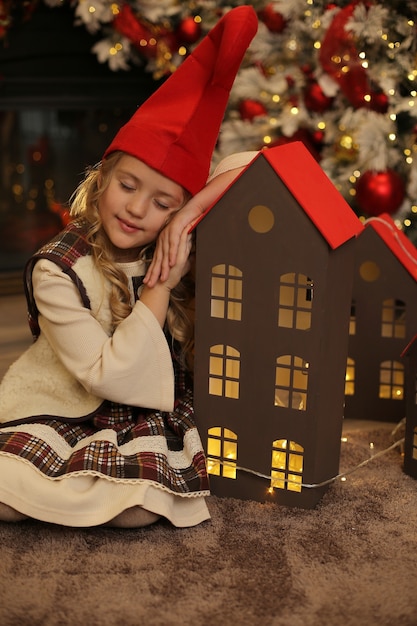 uma garota com fantasia de gnomo encostada em uma casa de madeira. Atmosfera de Natal de ano novo