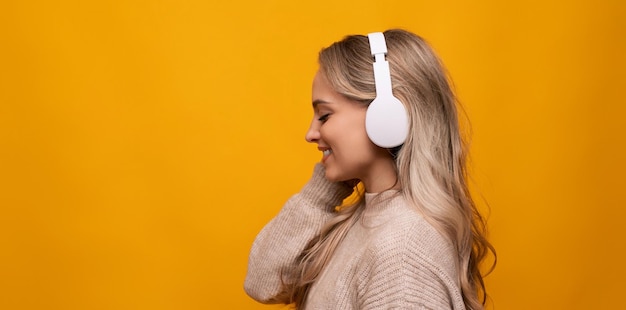 Uma garota com fones de ouvido grandes ouve sua música favorita em um fundo amarelo