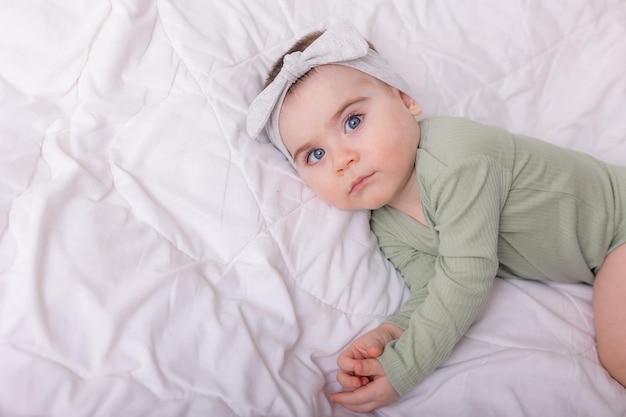 Uma garota com lindos olhos grandes está esfregando o bebê em casa na cama em uma roupa de algodão na roupa de cama branca