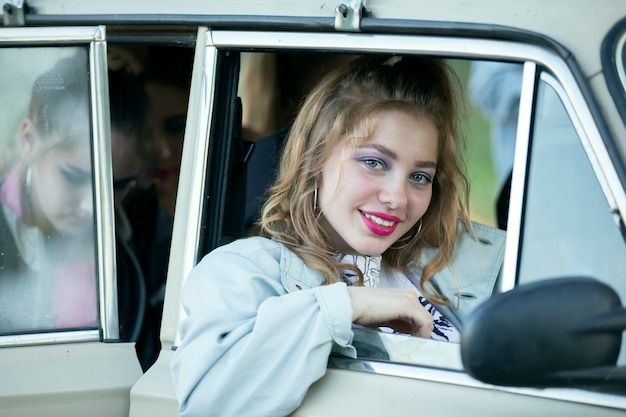 Uma garota com maquiagem brilhante olha pela janela de um carro retrô.