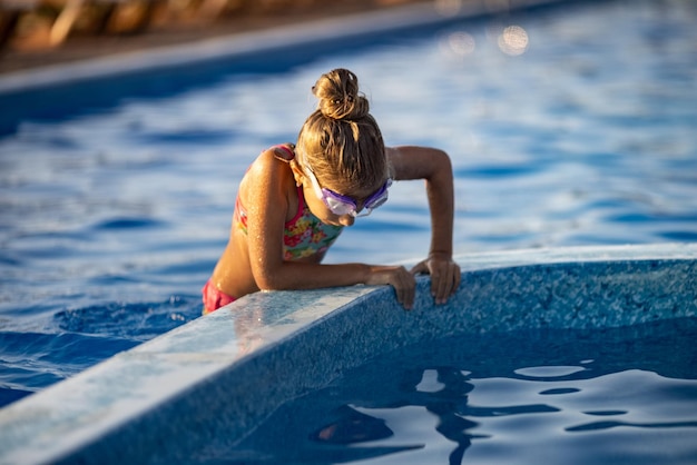 Uma garota com óculos de natação pula em uma piscina com água limpa no fundo de um pôr do sol quente de verão