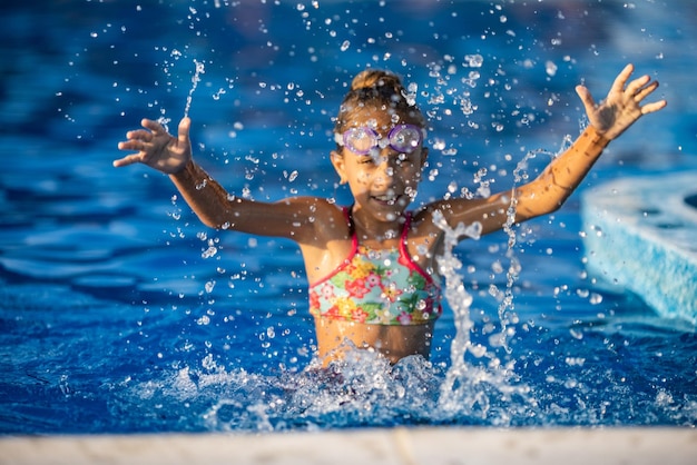 Uma garota com óculos de natação pula em uma piscina com água limpa no fundo de um pôr do sol quente de verão