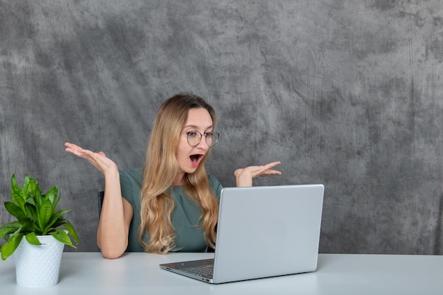 Uma garota com óculos e uma flor olha surpresa para o laptop Foto de alta qualidade