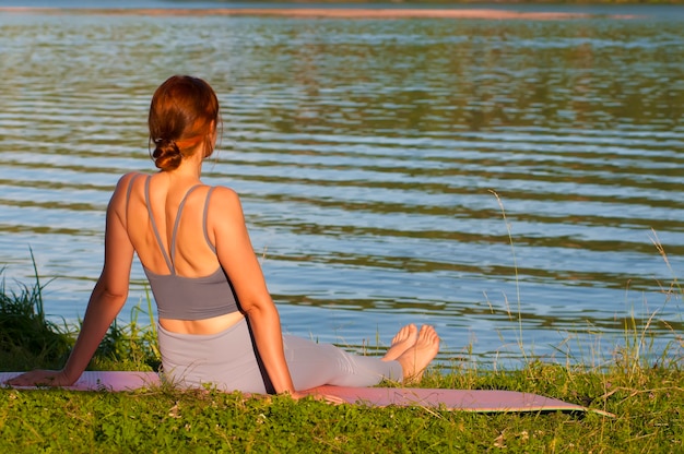 Uma garota com roupas esportivas está sentada na grama na margem do lago