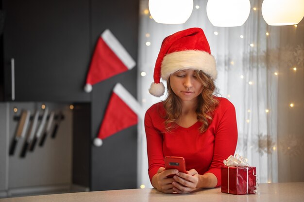 Uma garota com roupas vermelhas na cozinha olha para um smartphone na véspera de Natal