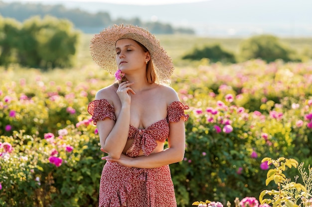 Uma garota com um chapéu de palha e um vestido vermelho caminha em um campo de rosas