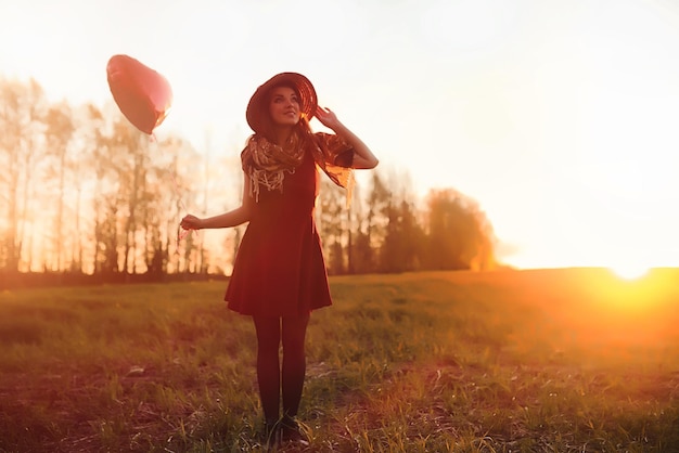 Uma garota com um chapéu em um passeio no parque. Uma garota com uma cesta entra no outono. Menina está caminhando pela estrada ao pôr do sol.