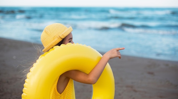 Uma garota com um círculo inflável amarelo à beira-mar Relaxando nas viagens de verão da praia