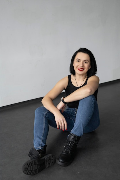 Uma garota com um corte de cabelo curto em botins e jeans senta-se no chão