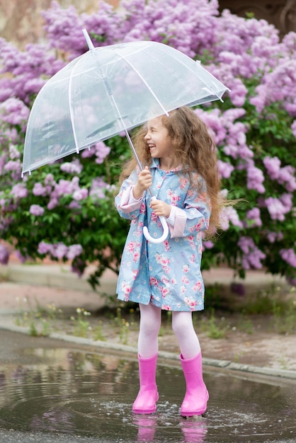 Uma garota com um guarda-chuva transparente no contexto de lilases florescendo gosta de primavera