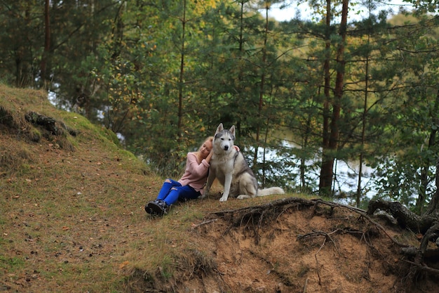 Uma garota com um husky caminha na floresta