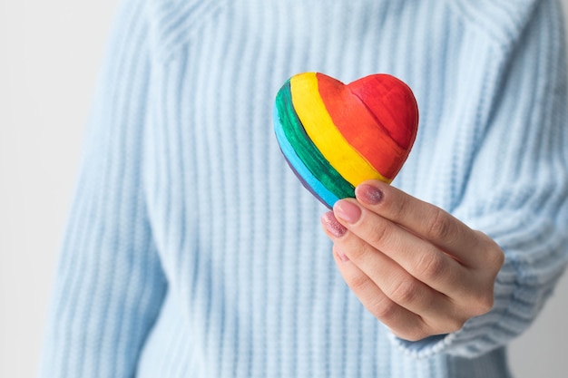 Uma garota com um suéter azul segura um coração multicolorido nas mãos, o conceito de LGBT amigável.