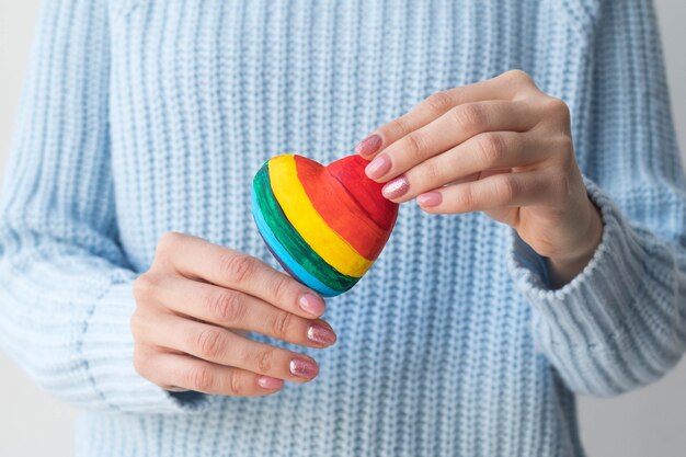 Uma garota com um suéter azul segura um coração multicolorido nas mãos, o conceito de LGBT amigável.