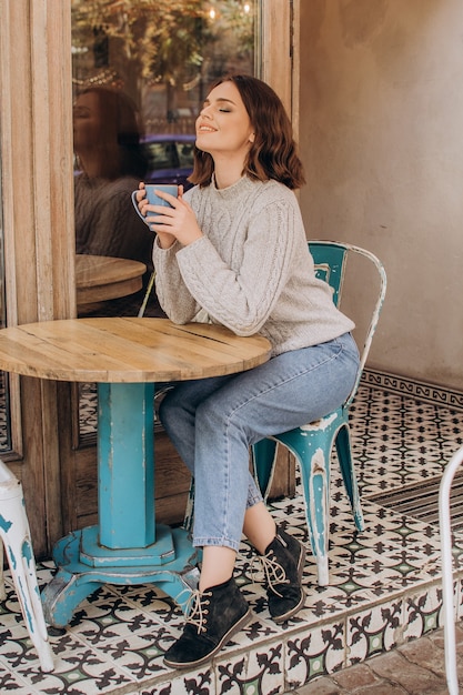 Foto uma garota com um suéter cinza se senta a uma mesa em um café, bebe chocolate e aprecia o aroma
