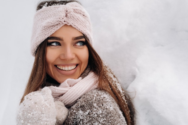 Uma garota com um suéter e luvas no inverno fica em um fundo coberto de neve