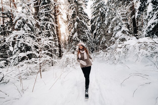 Uma garota com um suéter e óculos caminha na floresta coberta de neve no inverno