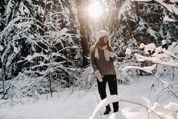 Uma garota com um suéter e óculos no inverno em uma floresta coberta de neve